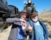 Two men use their hands to form the number 81 in front of steam locomotive 81