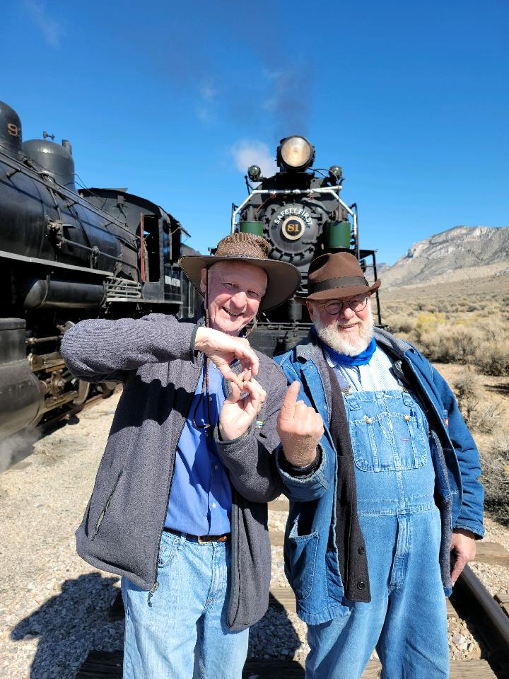 Two men use their hands to form the number 81 in front of steam locomotive 81