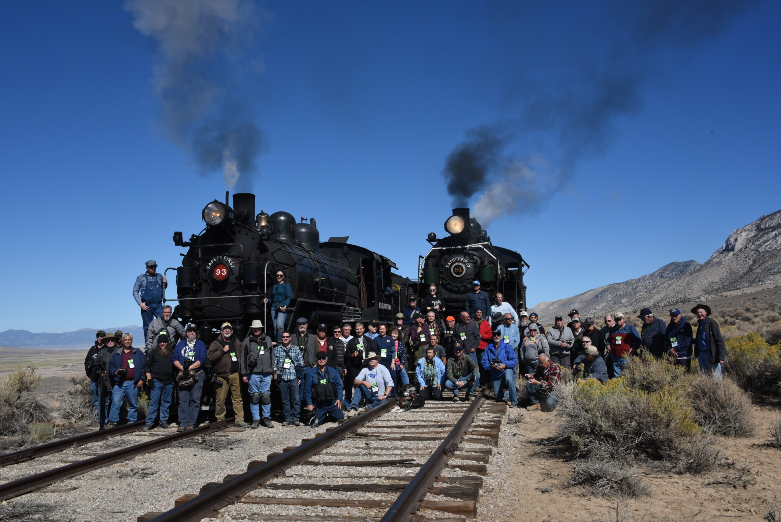 60 people gather around two steam locomotives to celebrate locomotive No. 81’s return and Trains Magazine’s 81st anniversary