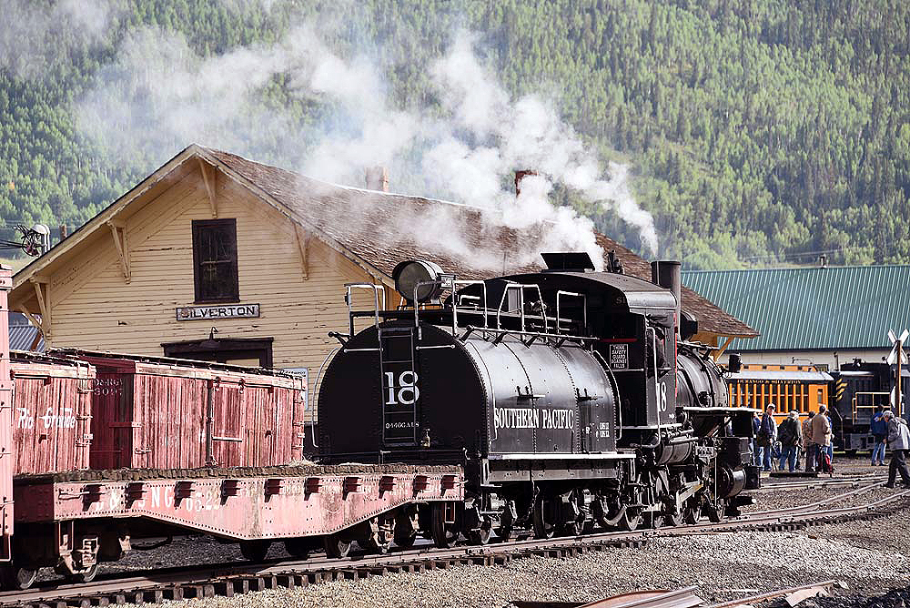 Rear view of a steam locomotive and tender in a rail yard.