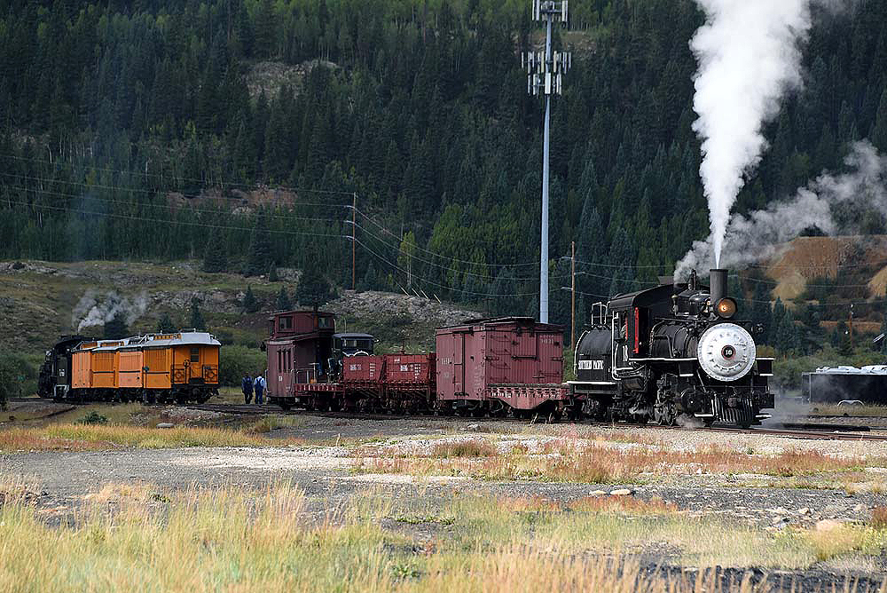 Two narrow gauge steam trains operated facing away from each other in a forested scene.