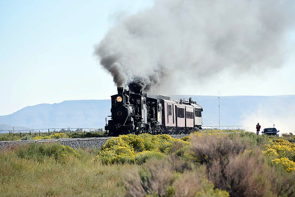 Double-headed steam passenger train high steps over the high plains.