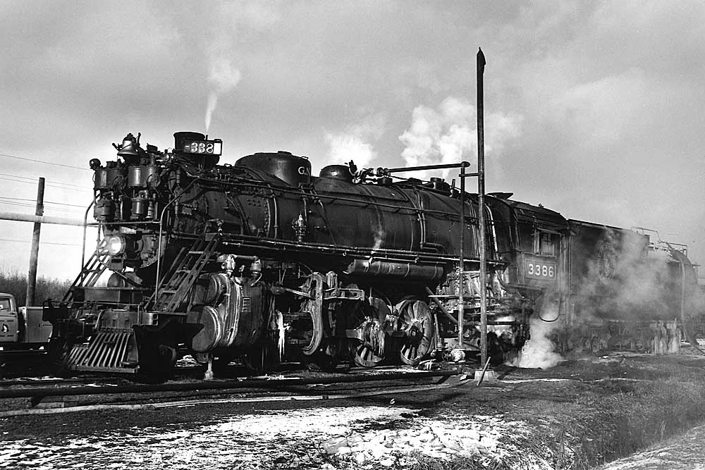 Steaming steam locomotive hooked up to stationary piping