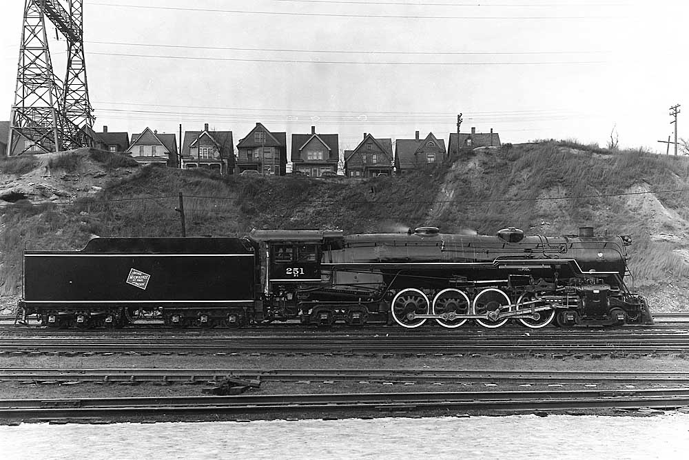Broadside of clean steam locomotive in valley in front of row of houses