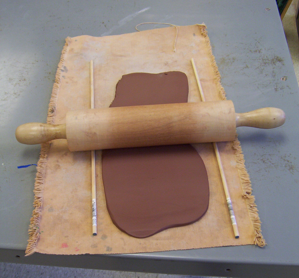 A rolling pin rolling out clay on a piece of canvas