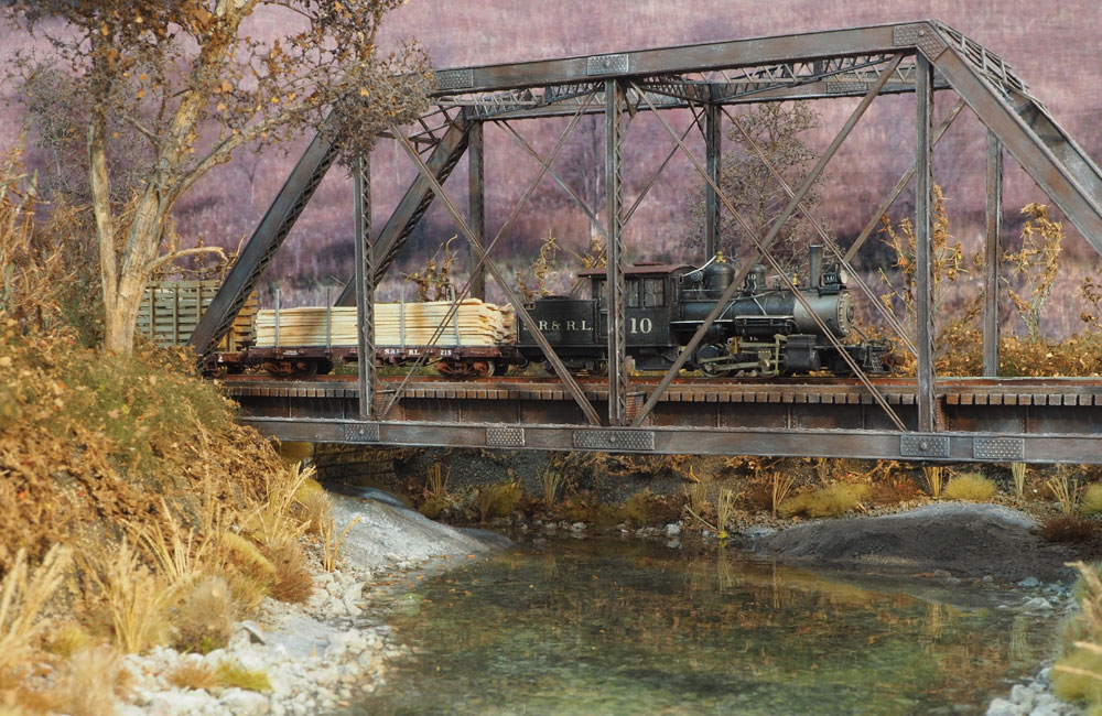 A geared steam locomotive leads a lumber train over a steel trestle above a creek