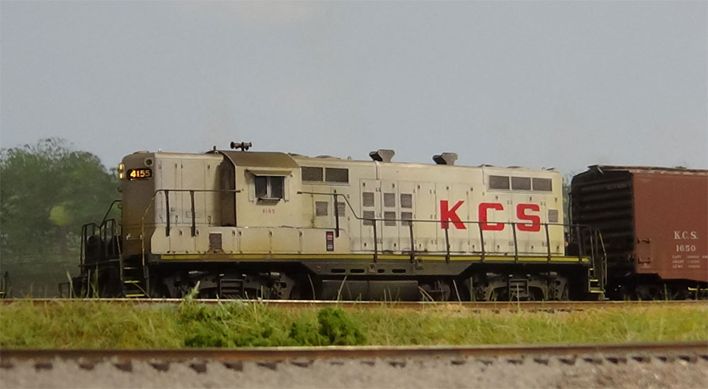 A white diesel with red “KCS” lettering pulls a boxcar