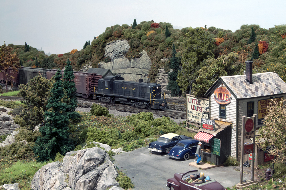 A train travels by a small diner in the mountainside