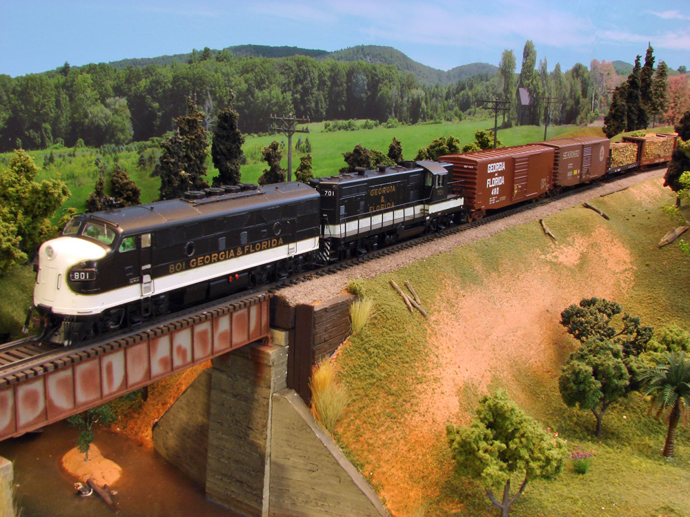 : A black-and-white F unit and a matching Geep pull a manifest freight onto a plate girder bridge