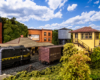 A dark green Pennsylvania Railroad F unit passes a wooden station and a switch tower in a suburban scene