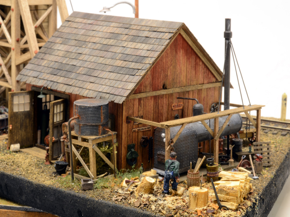 A worker carries freshly chopped firewood to a former locomotive boiler behind a mine building