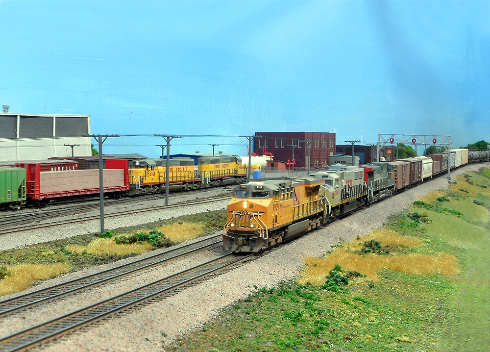 A foreground yellow Union Pacific freight train splits a distanct signal bridge in a relatively flat scene in N Scale.