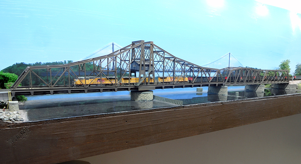 A yellow Union Pacific freight train crosses a bridge on a model train layout.