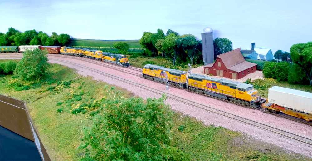 Two freight trains meet in a rural scene on a model train layout.