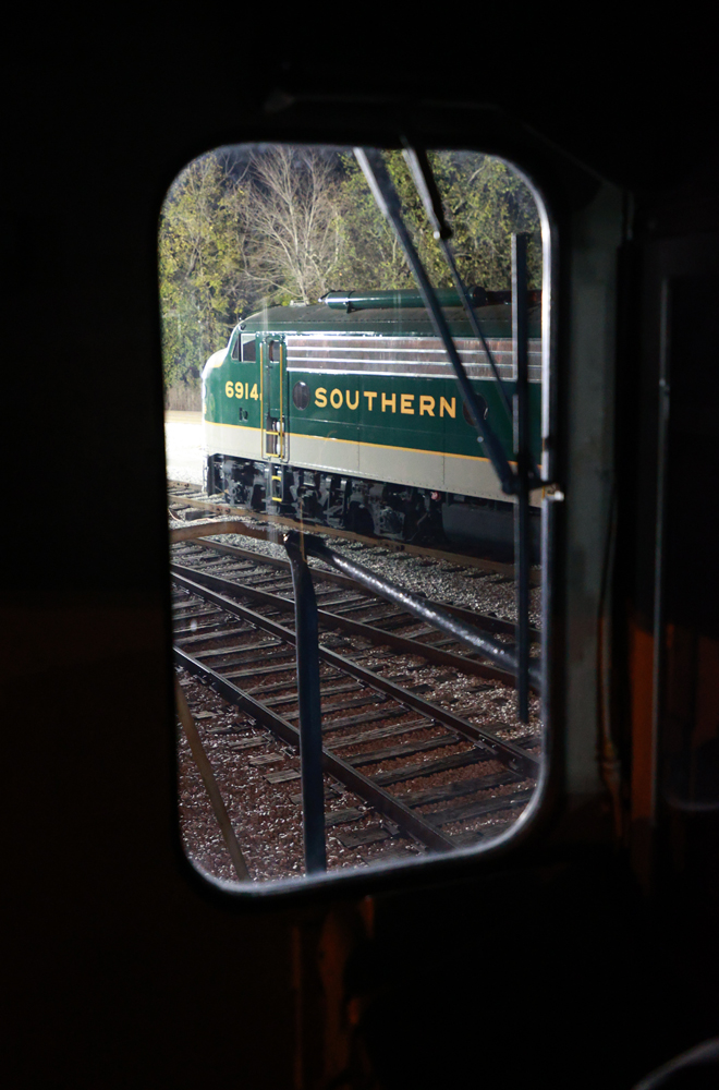 Green and white streamlined diesel as viewed through cab window of another locomotive