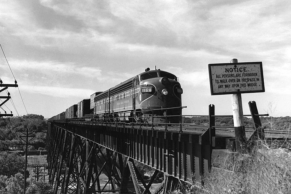Streamlined diesel locomotives lead freight train on high steel bridge.