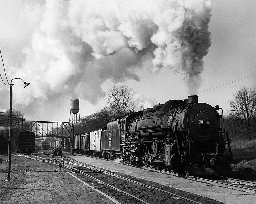 Smoking steam locomotive leads freight train under bridge