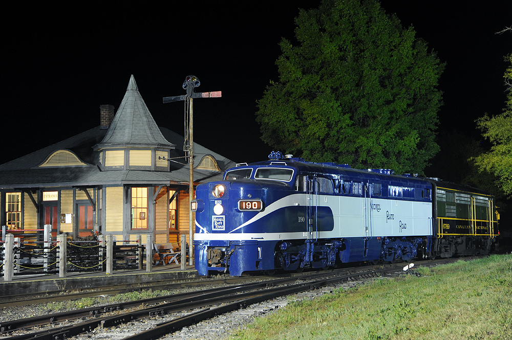 Top preserved diesel locomotives: Blue and white diesel locomotive at night in front of a lighted depot.