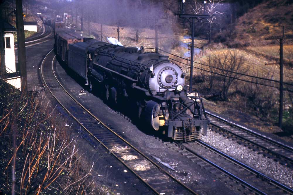 Steam locomotive leads freight train through curve by white tower