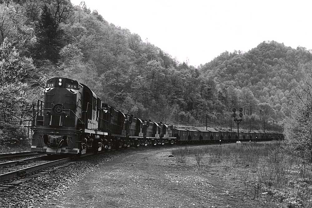 Five diesel locomotives roll a loaded coal train around a curve past some signals