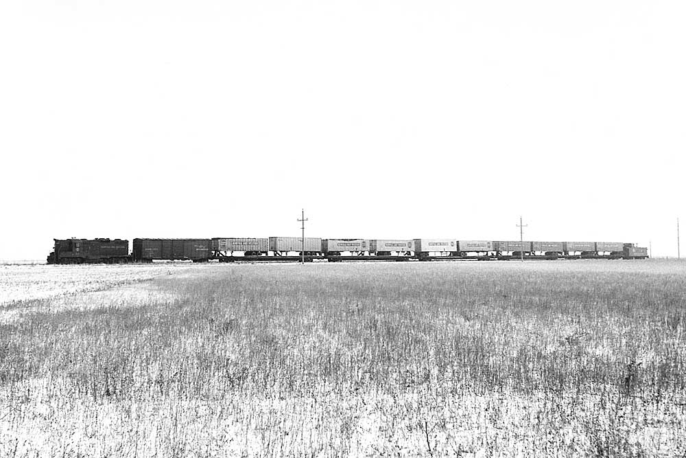 Diesel locomotive with one boxcar and many flatcars with trailers in profile