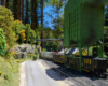 A modern diesel in a military camouflage paint scheme moves coal gondolas under a green coal loader