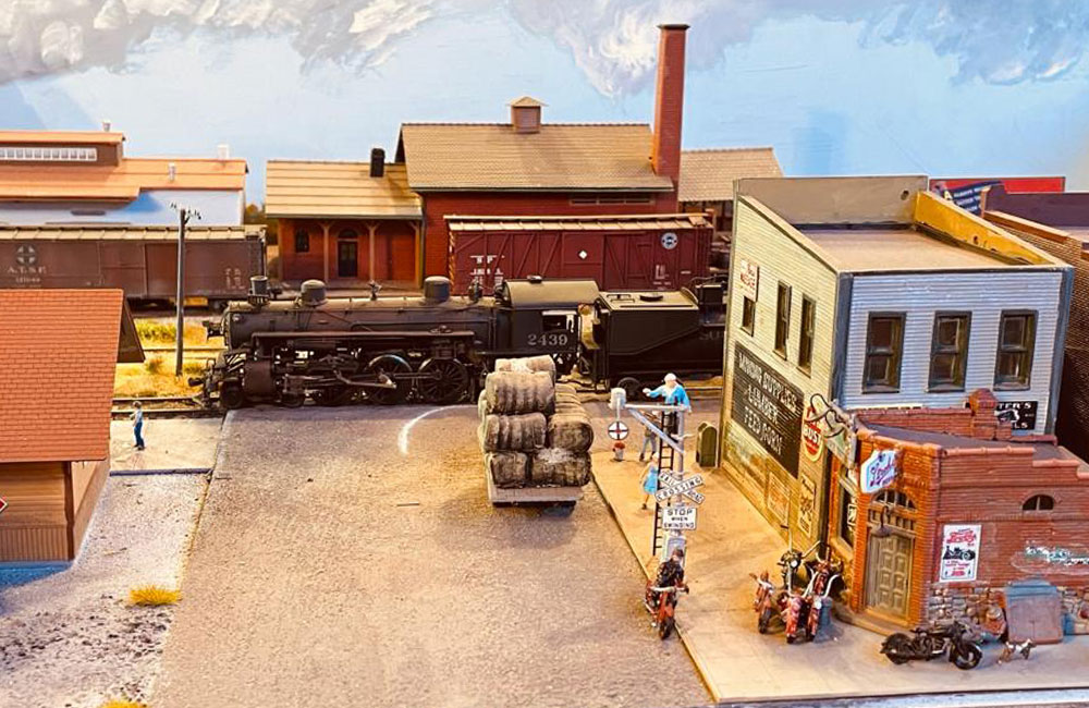 A steam locomotive crosses the road while a group of motorcyclists pulls up to a bar