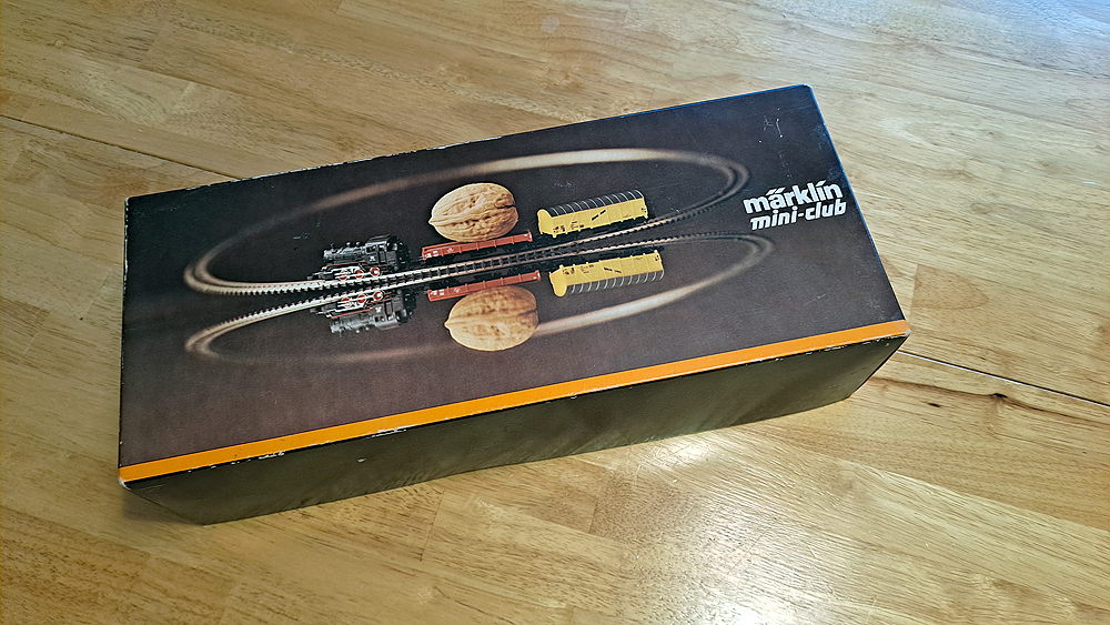 Brown Märklin Mini-Club train set box, 0-6-0 tank engine, red four-wheel flat car carrying walnut, yellow four-wheel banana boxcar.