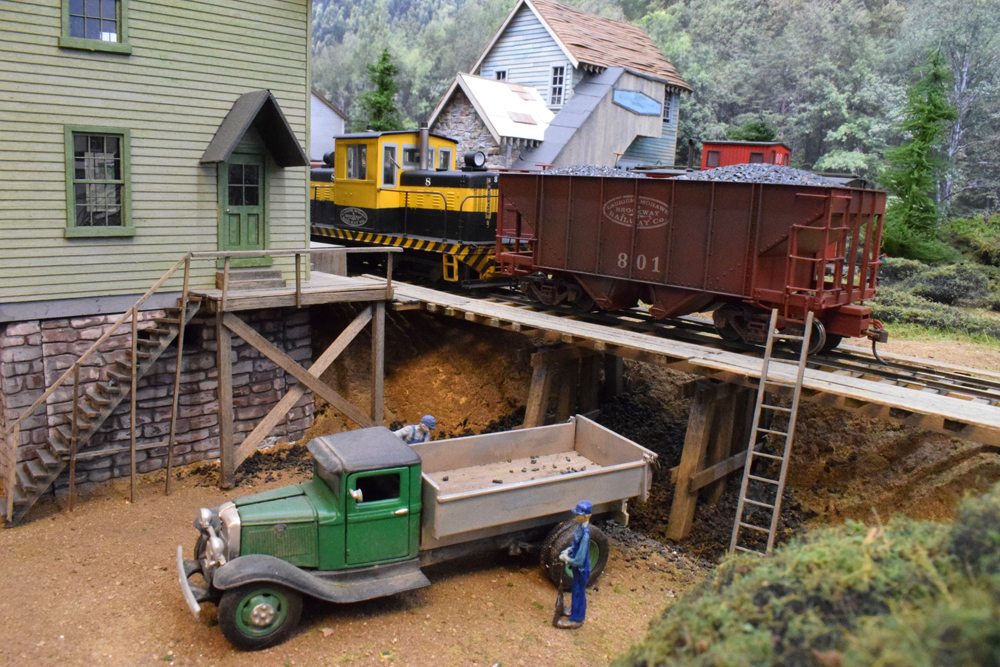 yellow model diesel engine with load of coal and model truck on a layout scene