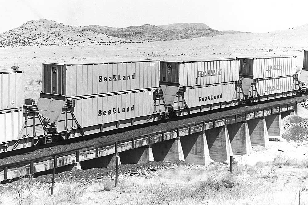 Early container train passes over low concrete bridge