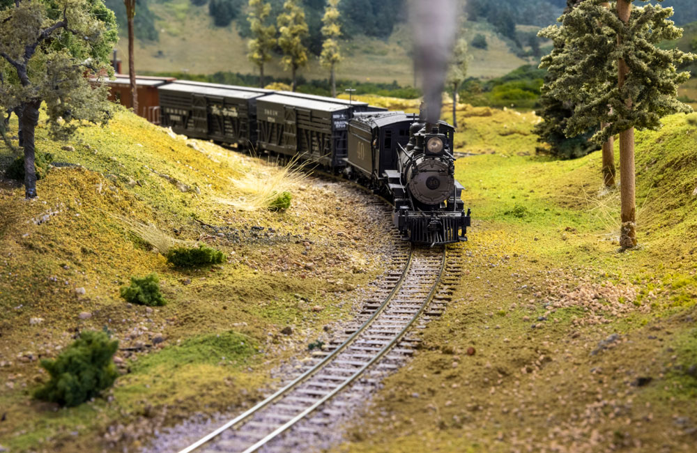 A narrow gauge steam locomotive rounds a curve with stock cars in tow