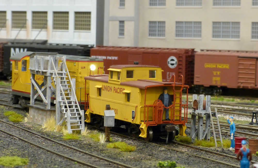 A gray-and-yellow diesel switcher shoves a matching-color caboose up to a servicing platform