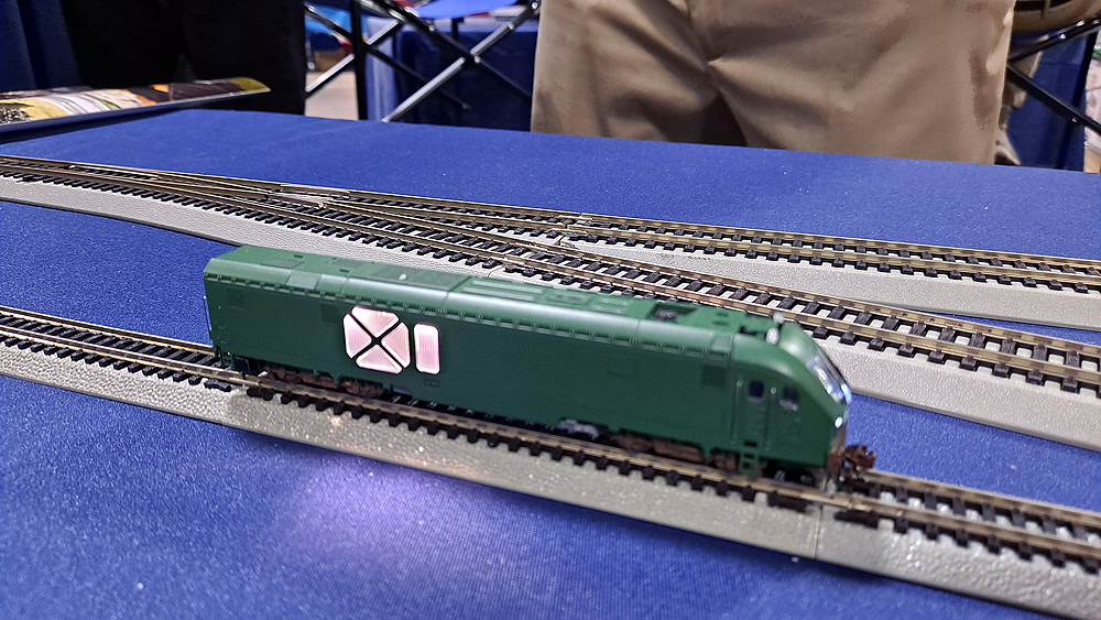 Green locomotive with lighted panel on side, sitting on gray and black plastic track.