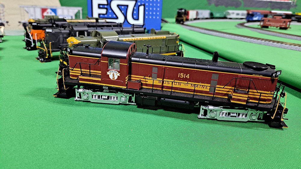 Locomotive with maroon sides with yellow stripes and black roof and top surfaces, silver trucks.