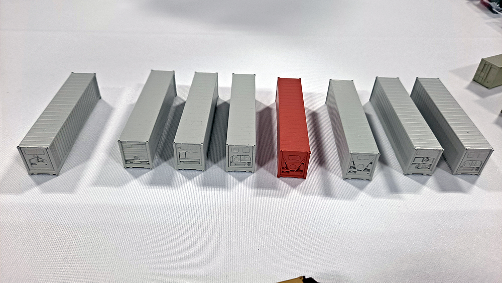 Seven gray and one brick red preproduction N scale container samples are shown on a white tablecloth.