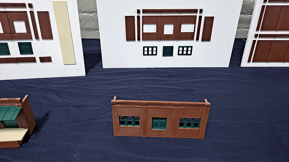 Structure walls and doors are mounted to a white board, with the assembled parts laying in front of the board on a table.