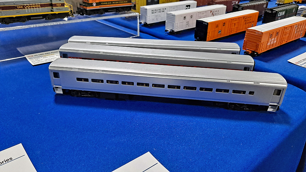 Three silver passenger coaches on blue tablecloth with white and orange mechanical refrigerator cars in the background.