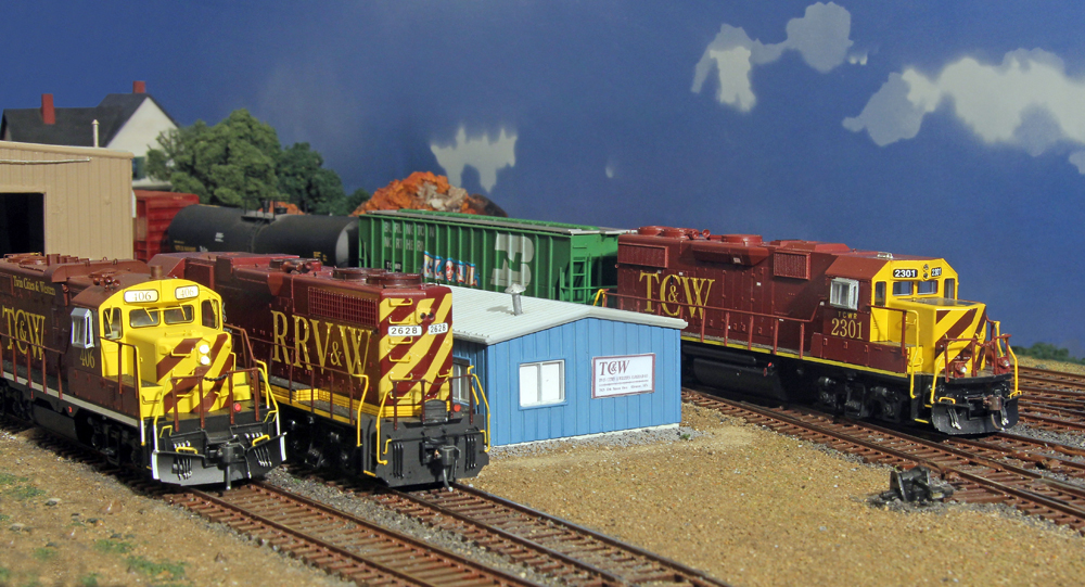HO scale diesel locomotives, freight cars, and buildings on a scenicked layout.