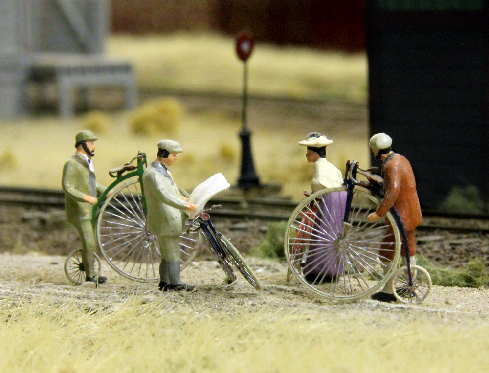 HO scale figures and 1890s-style bicycles on a model railroad.