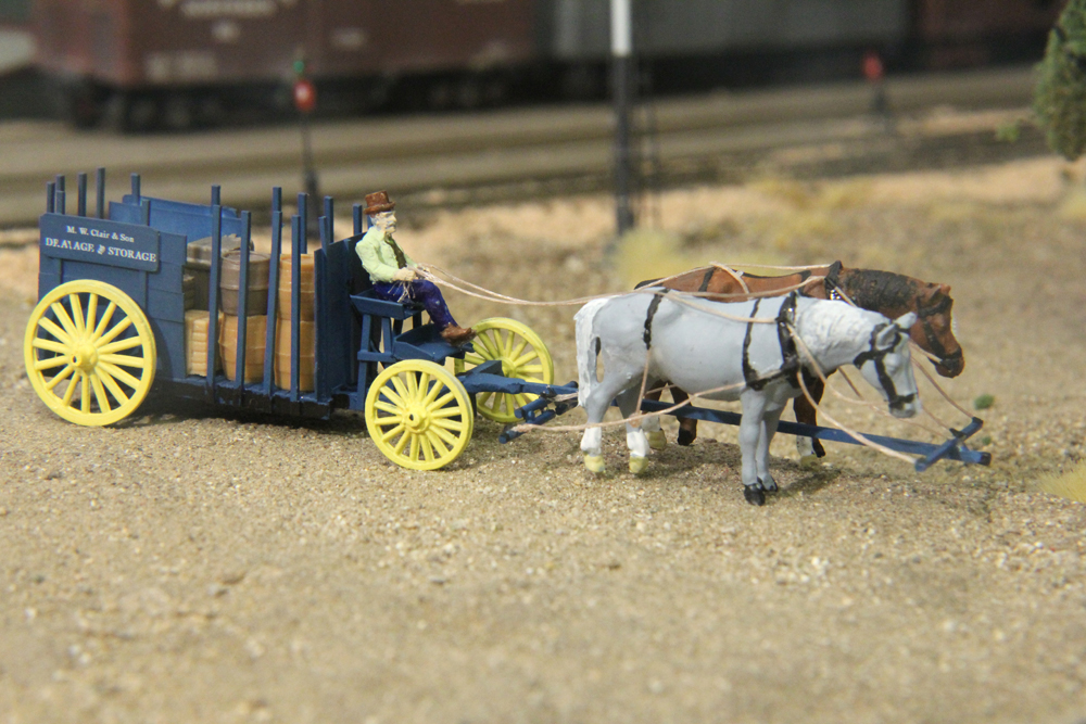 Two horses pulling man and wagon on an HO scale model railroad.