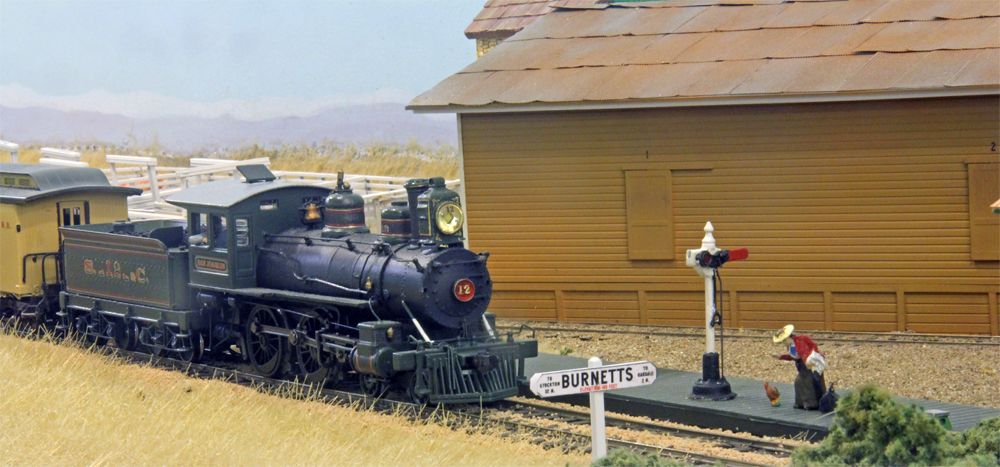 Steam powered passenger train approaching platform with signal, woman carrying luggage, and chicken.