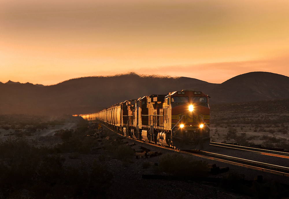 Train of covered hoppers in golden light with orange sky