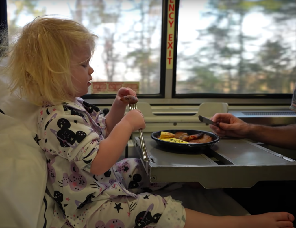 Baby girls eats food at a tray table on a train.