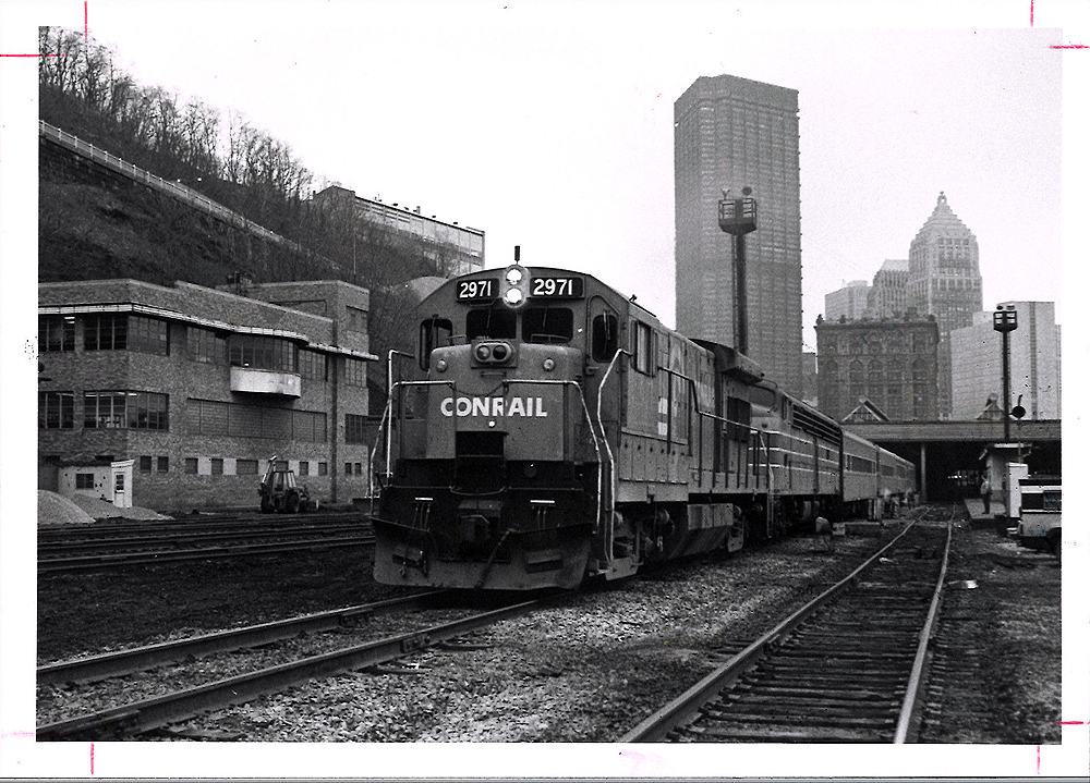 Conrail passenger trains: Locomotive leads a train away from a big-city downtown.