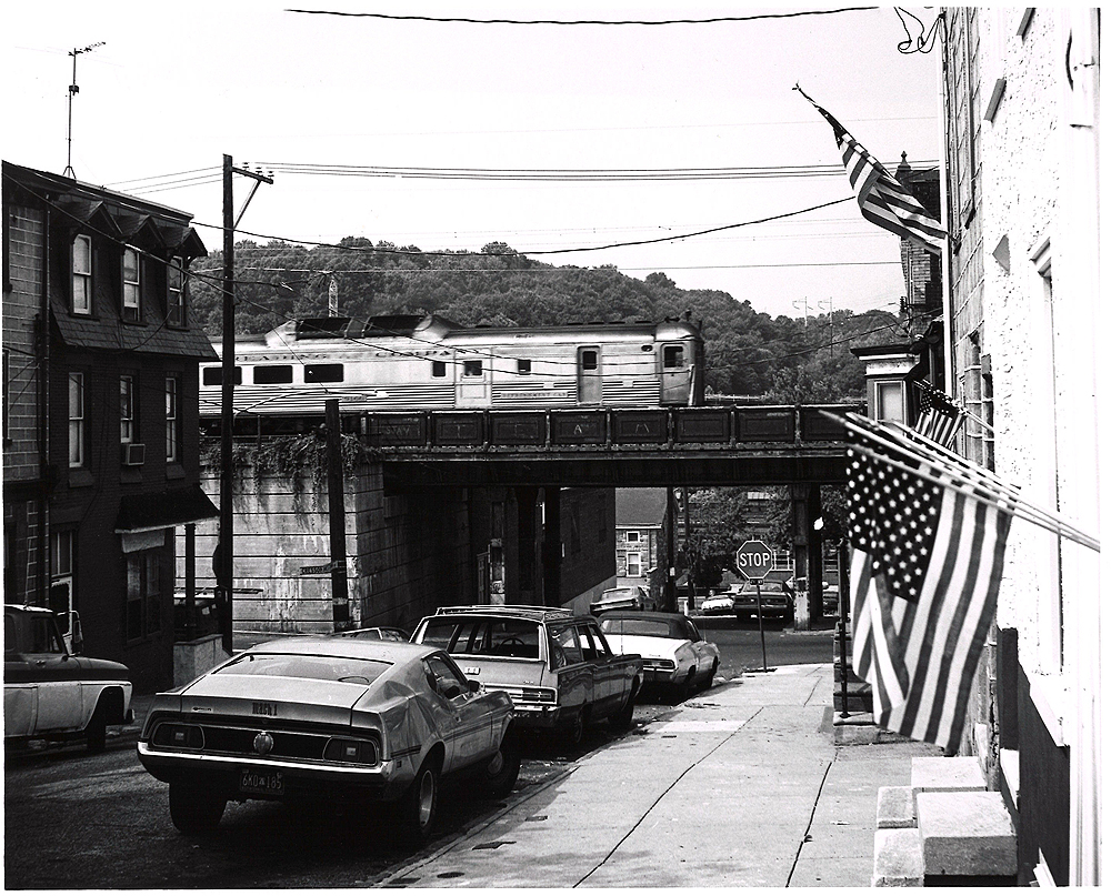 Conrail passenger trains: A rail diesel car runs on a bridge in a neighborhood.