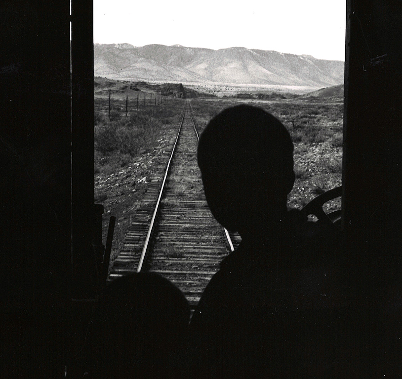 Silhouette of a man looking out the door of a passenger car.