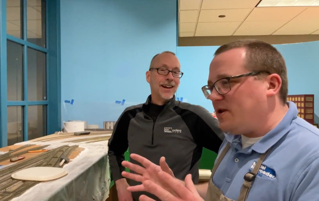 Two men talking near a model railroad layout.