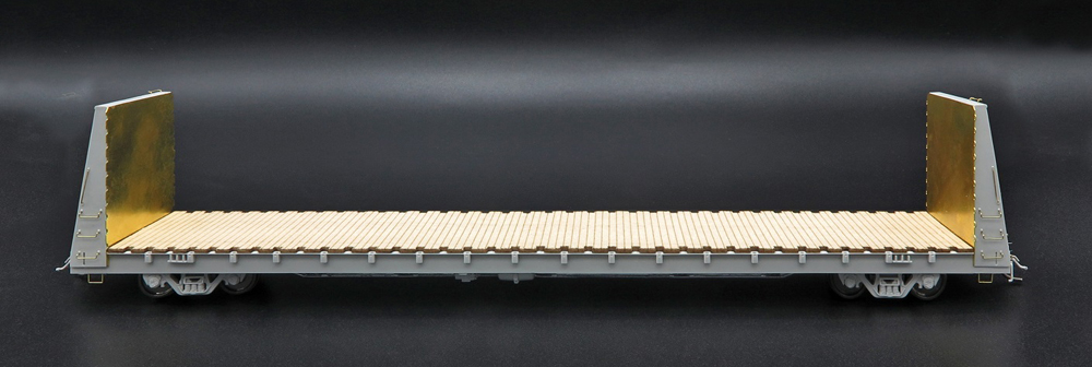 Photo of pre-production bulkhead flatcar painted gray with unpainted wood deck and brass ends on black background.