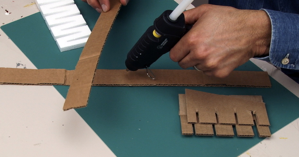 Trains.com producer uses hot glue gun to fasten together cardboard strips on a workbench