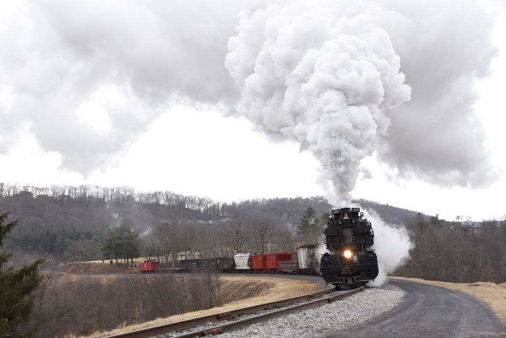 Big plume above black steam engine coming around a bend